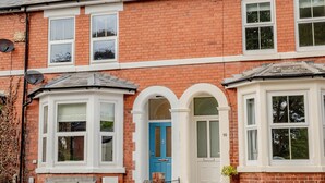 A two-story brick house with a blue front door, white-framed windows, and a chimney. - Exquisite renovation in central location (Hereford)