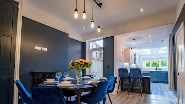 A modern dining area with a dark blue wall, a large window, and a view of the kitchen. - Exquisite renovation in central location (Hereford)