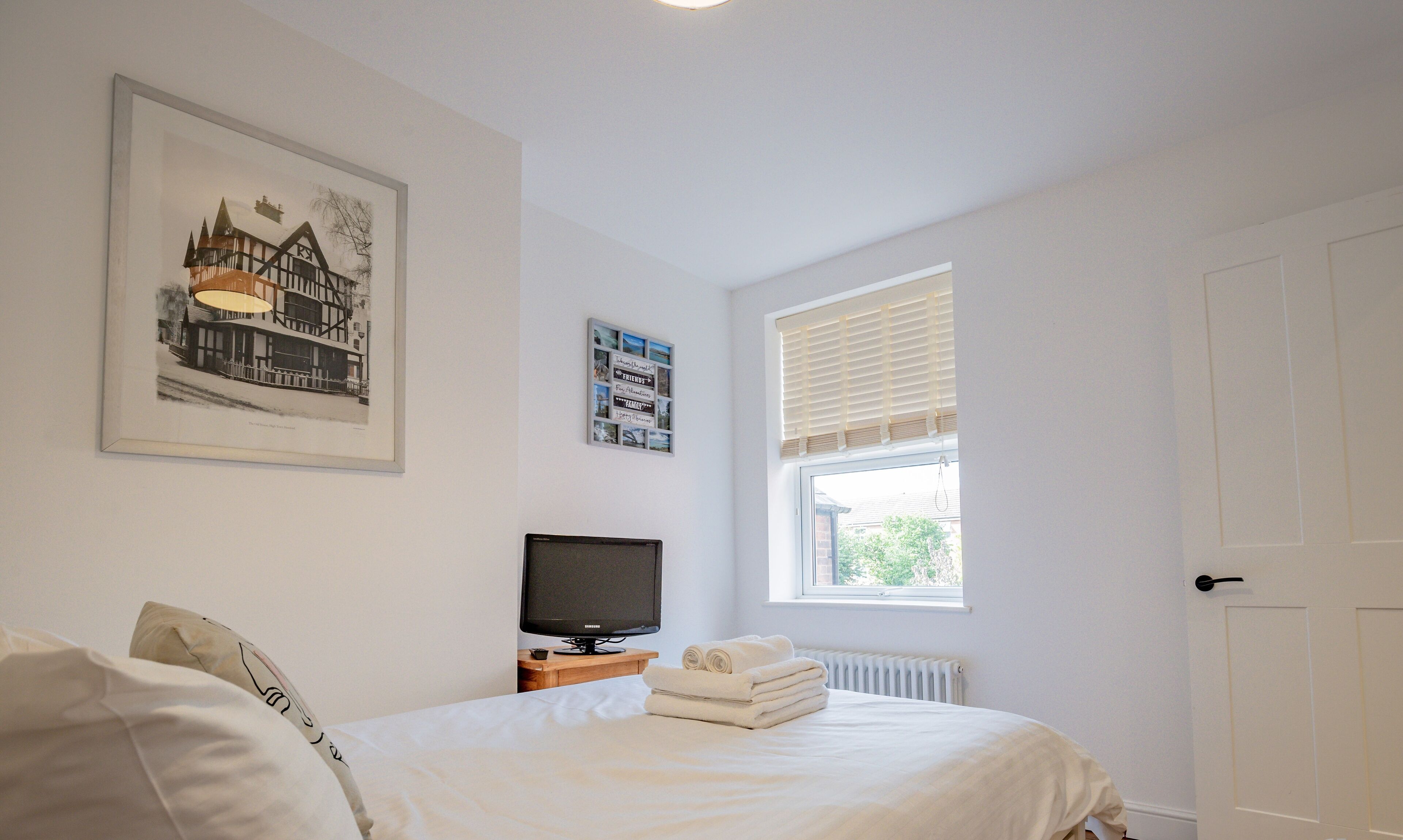 A bedroom with a bed, a television, a window, and a door.