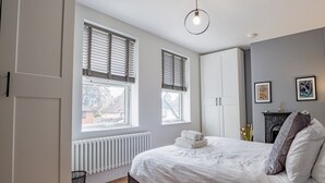 A bedroom with a bed, two windows with blinds, a radiator, a wardrobe, and a hanging light fixture. - Exquisite renovation in central location (Hereford)