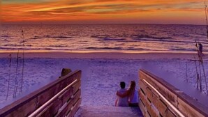 A wooden pier leading to a beach with a sunset in the background.