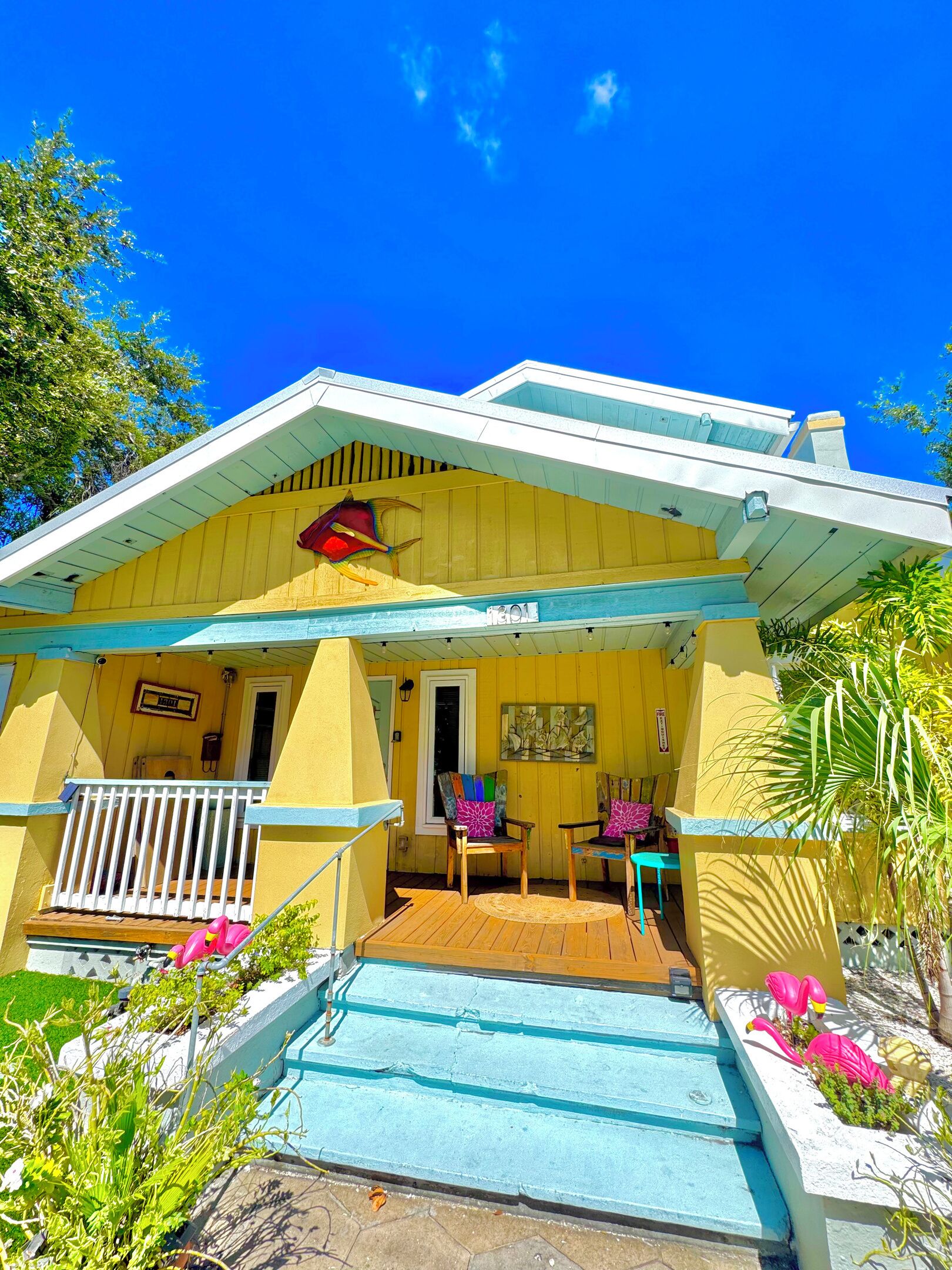 A yellow building with a covered porch, a small pool, and colorful chairs.