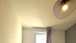 A room with a wooden dining table, a gray chair, a ceiling light fixture, and a window with curtains.
