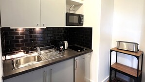A modern kitchen with grey cabinets, a black tiled backsplash, a stainless steel sink, a microwave, and a toaster on a wooden shelf.