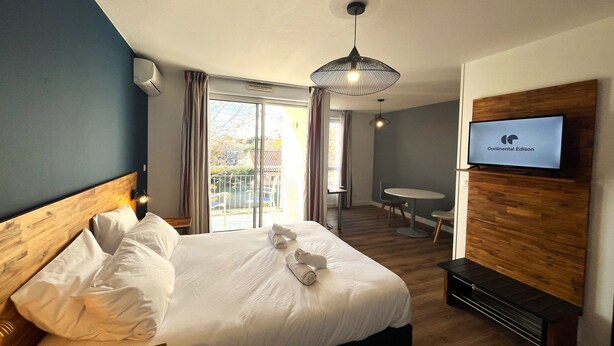 A hotel room with a bed, a TV, a desk, and a view of the outside.