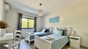 Un dormitorio con dos camas individuales, un escritorio, una silla, una mesita de noche y una lámpara colgante.