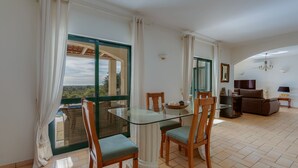 Uma sala de jantar com mesa de vidro e cadeiras de madeira, um sofá e vista através de uma grande janela.