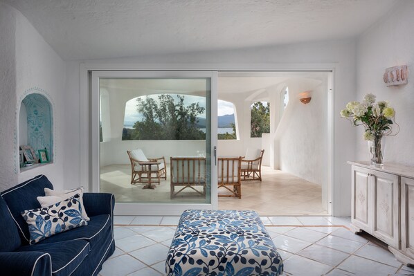 Una habitación moderna con un sofá azul, un reposapiés estampado y vistas a un balcón con mobiliario exterior.