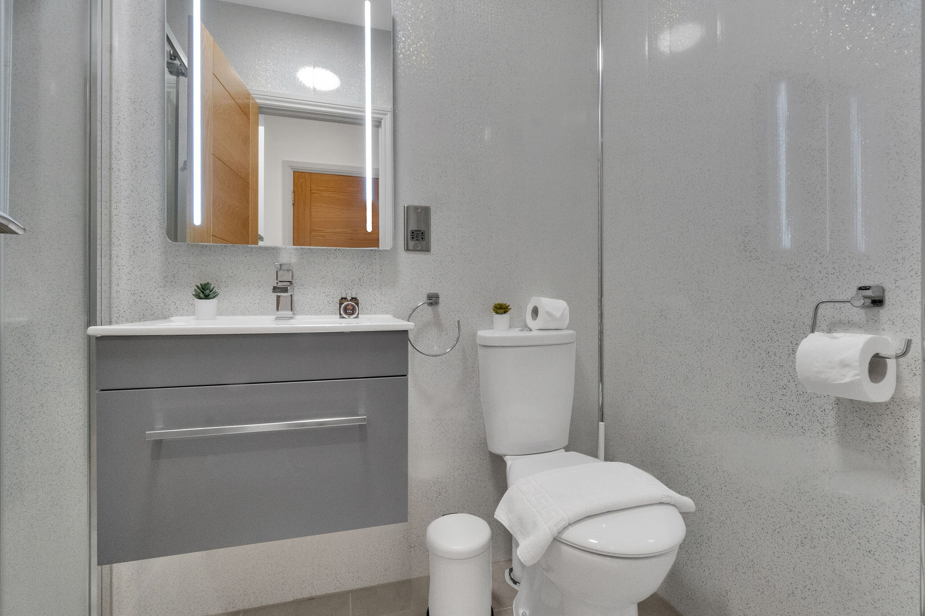 A modern bathroom with a grey vanity, a toilet, and a glass shower enclosure.