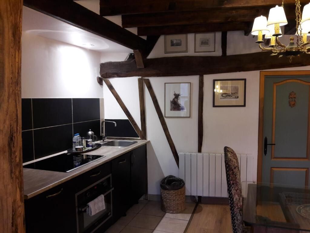 A kitchen with a black countertop, white tiles, a wooden ceiling, and a radiator.