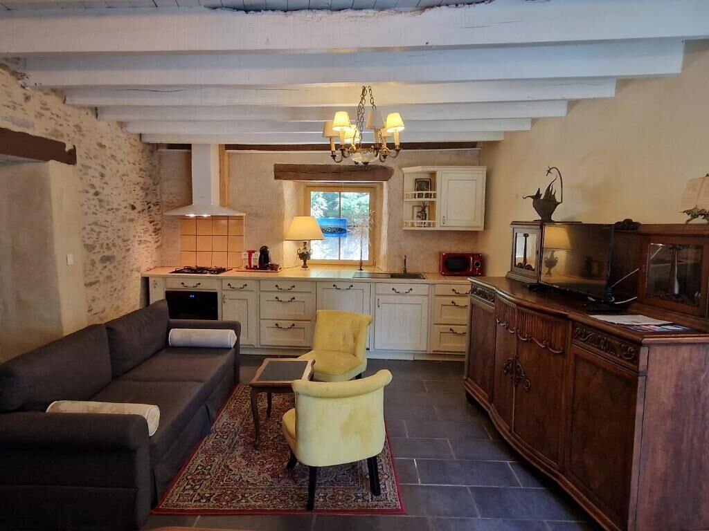 A cozy living room with a sofa and armchairs, a kitchen with white cabinets and a chandelier, and a wooden cabinet with a television.