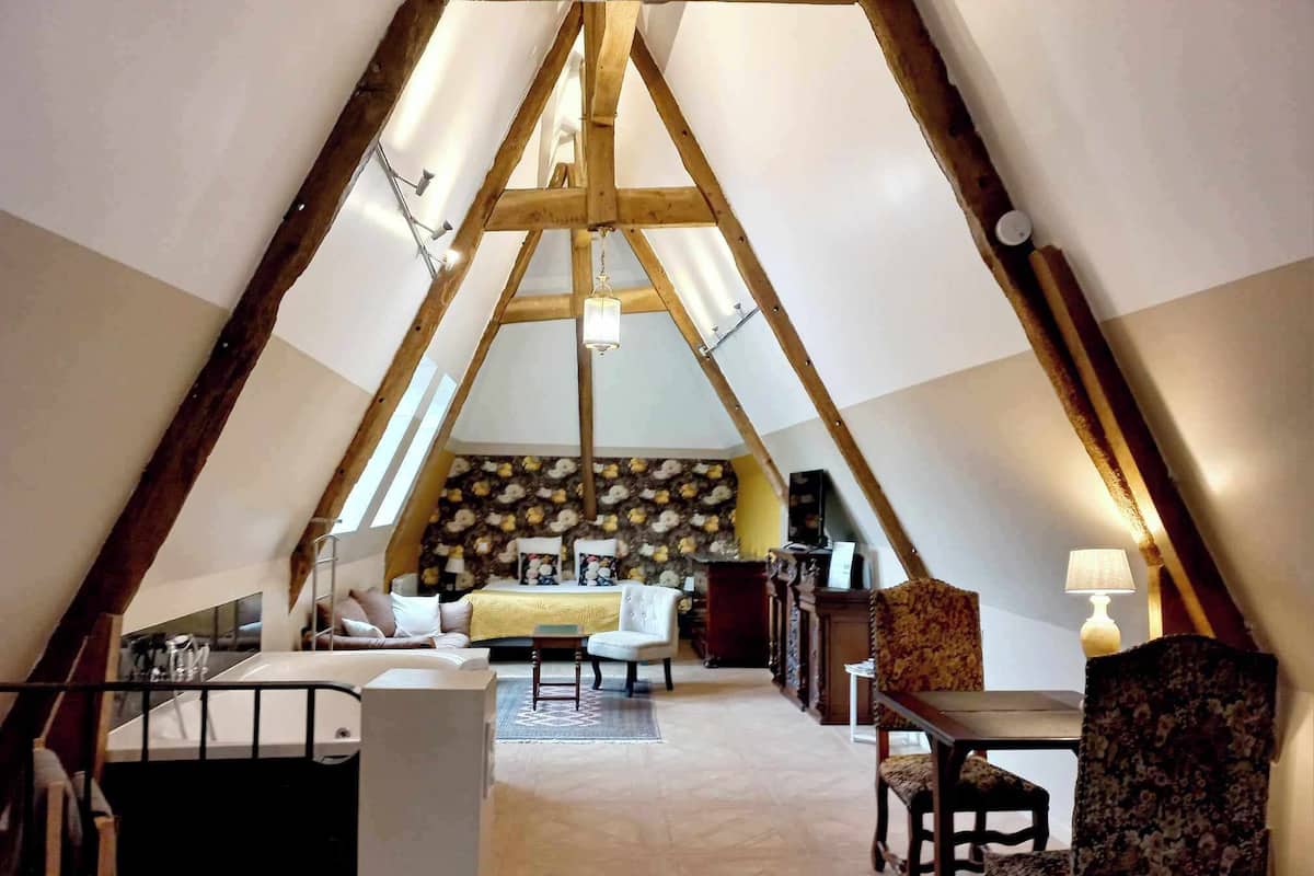 Um quarto aconchegante em formato triangular, com cama, área de estar e uma mesa.