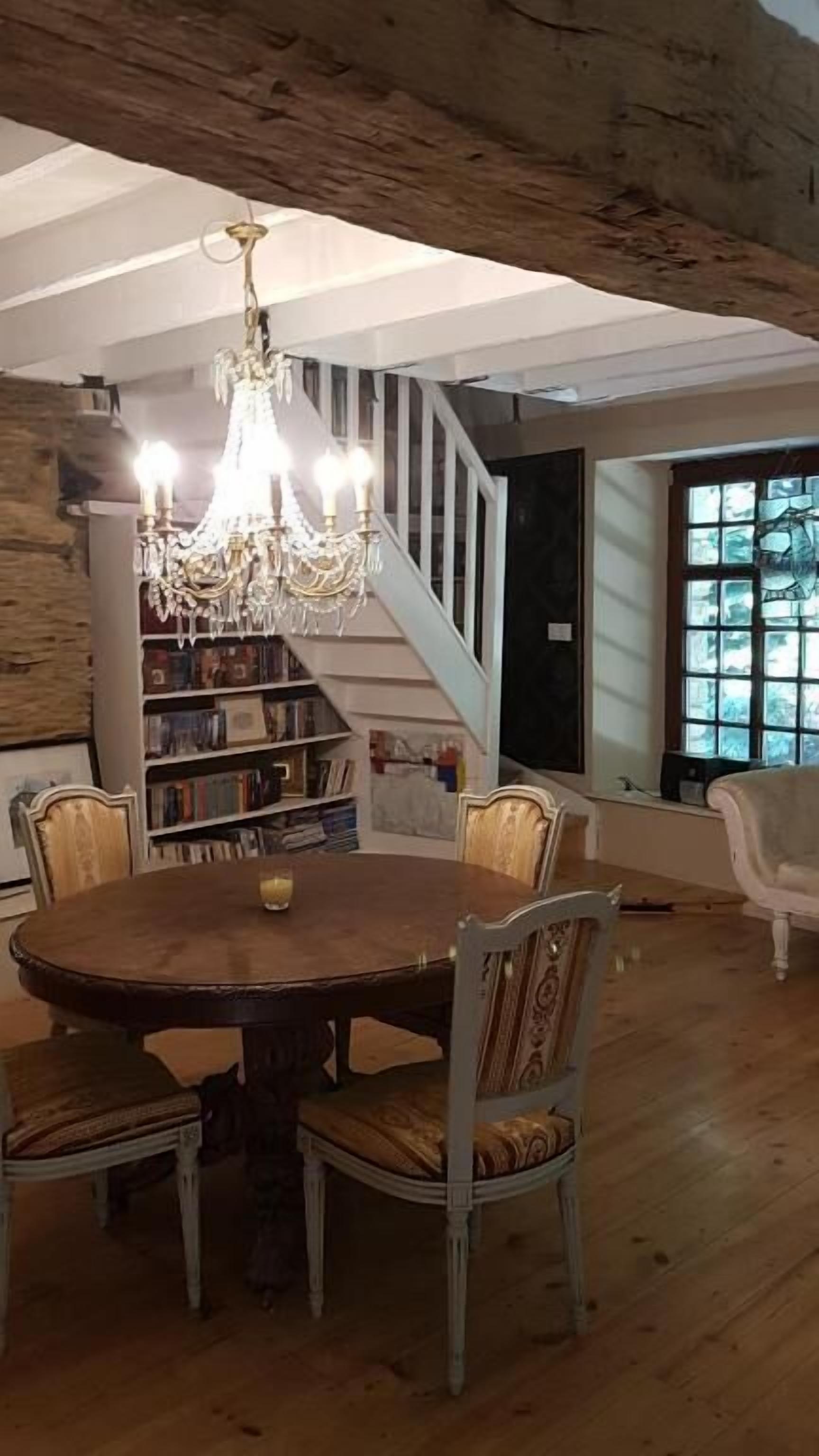 Un espace repas avec une table et des chaises en bois, un lustre et un escalier menant à un autre niveau.
