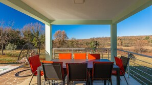 An outdoor patio with a table and chairs, a view of the countryside, and a railing.