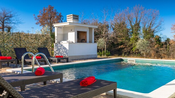 A swimming pool with lounge chairs and a small structure, likely a changing room or storage, surrounded by trees. - Villa Petar by Villas Guide (Buroli)