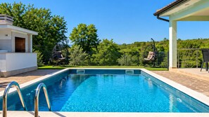 A swimming pool with a clear blue water, surrounded by a patio area with chairs and a covered seating area. - Villa Petar by Villas Guide (Buroli)