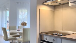 A modern kitchen with a built-in stove, a dining area with a round table and chairs, and a window with sheer curtains. - Villa Petar by Villas Guide (Buroli)