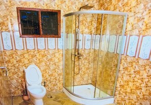 A bathroom with a glass-enclosed shower, a toilet, and a window with decorative paper.