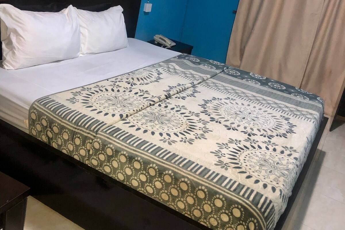 A bedroom with a bed, a bedside table, a wall-mounted fan, and curtains.