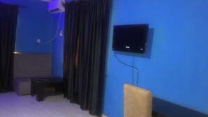 A room with a blue wall, a flat-screen TV mounted on the wall, a sofa, a small table, and a chair. - Prince Palace Hotel (Lagos)