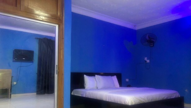 A bedroom with a bed, a TV mounted on the wall, and a ceiling fan. - Prince Palace Hotel (Lagos)