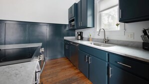 A modern kitchen with dark blue cabinets, a stainless steel sink, and a built-in oven. - Cozy 2BR Carriage in the heart of Downtown! (Charleston)