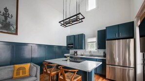 A modern kitchen with dark blue cabinets, a stainless steel refrigerator, and a central island with chairs. - Cozy 2BR Carriage in the heart of Downtown! (Charleston)
