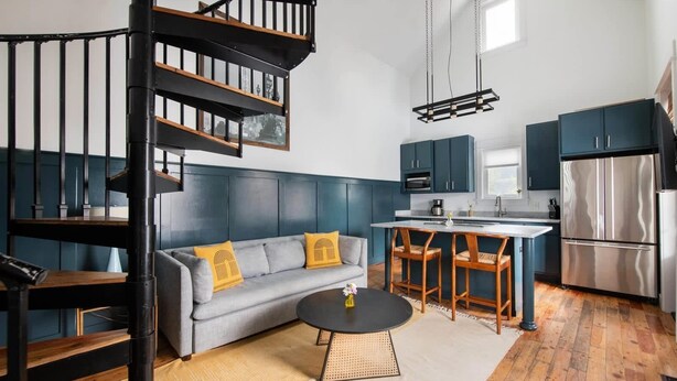 A modern kitchen with dark blue cabinets, a stainless steel refrigerator, and a dining area with a round table and two chairs. - Cozy 2BR Carriage in the heart of Downtown! (Charleston)