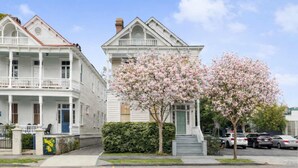 Een wit huis met twee verdiepingen en een balkon, omringd door een verzorgd gazon en een boom met roze bloemen.