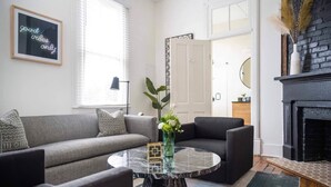 Een woonkamer met een grijze bank, een zwarte fauteuil, een marmeren salontafel en een open haard.