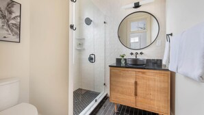 Een moderne badkamer met een douchecabine van glas, een houten wastafelmeubel en een ronde spiegel.