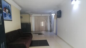 A living room with a dark brown sofa, a flat-screen TV mounted on the wall, and a tiled floor. - Icon valley Hotel limited (Abuja)