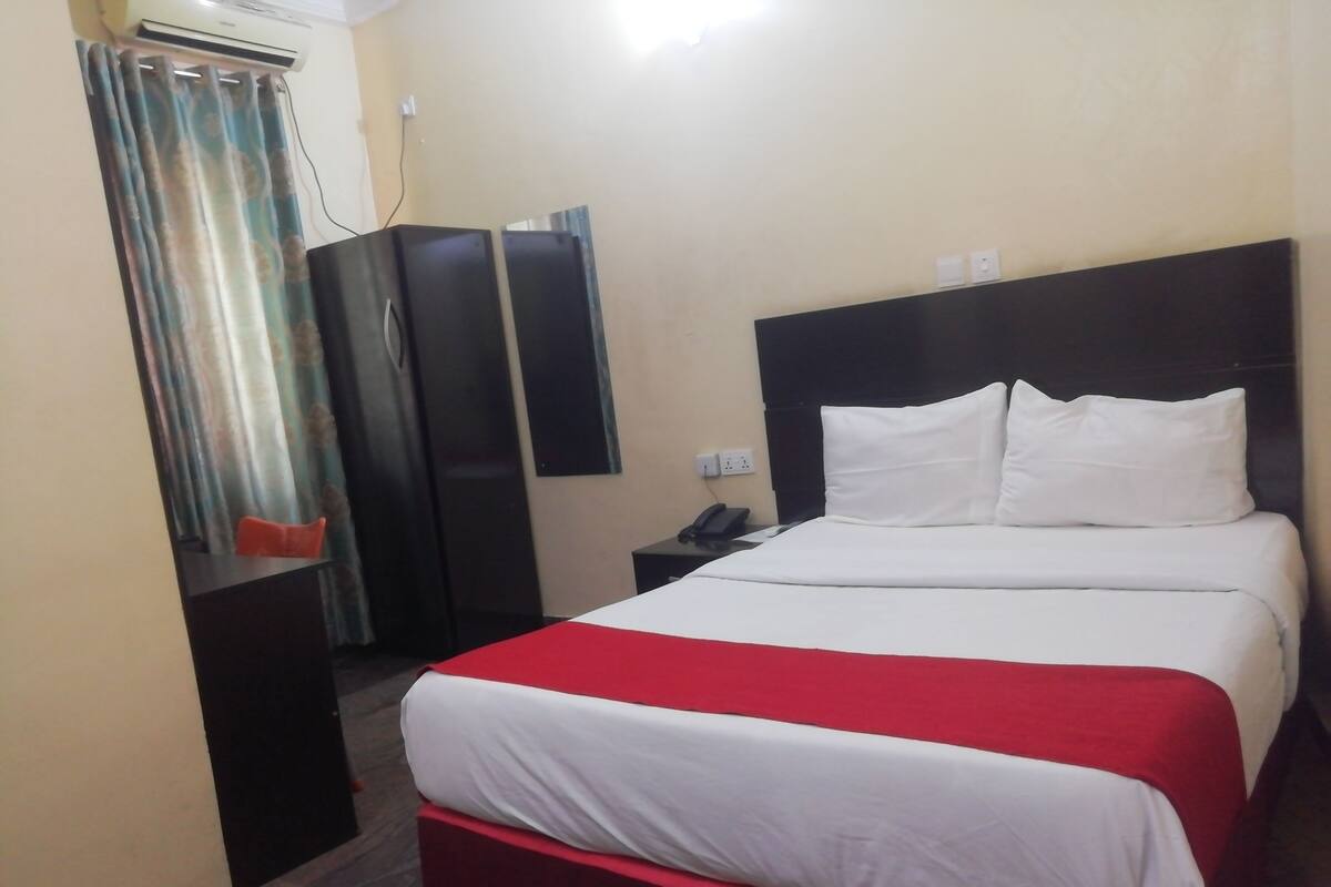 A hotel room with a bed, a nightstand, a phone, a wardrobe, and a curtain.