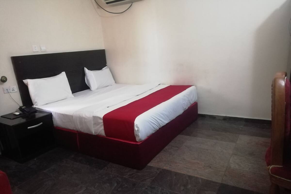 A hotel room with a bed, a nightstand, and a chair.