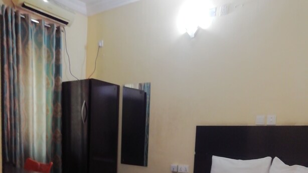 A hotel room with a large bed, a wardrobe, a desk, and an air conditioning unit. - Icon valley Hotel limited (Abuja)