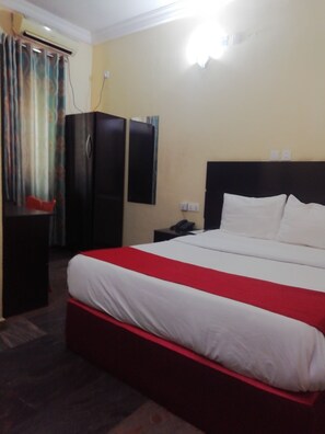 Habitación de hotel con una cama grande, un armario, un escritorio y un equipo de aire acondicionado.