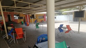 A covered outdoor seating area with multiple tables and chairs, a television screen, and a vending machine. - Icon valley Hotel limited (Abuja)