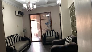 A living room with two sofas, a chair, a chandelier, and a sliding glass door leading to a balcony. - H18 Apartment (Abuja)