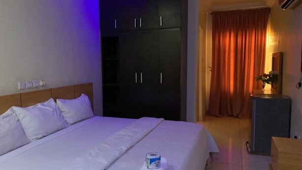A hotel room with a bed, a wardrobe, a desk, and a curtain. - H18 Apartment (Abuja)