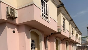 A building with pink walls and multiple windows, featuring air conditioning units on the exterior. - H18 Apartment (Abuja)