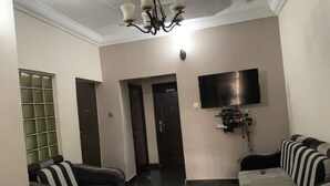 A living room with a sofa, armchairs, a TV mounted on the wall, and a chandelier. - H18 Apartment (Abuja)