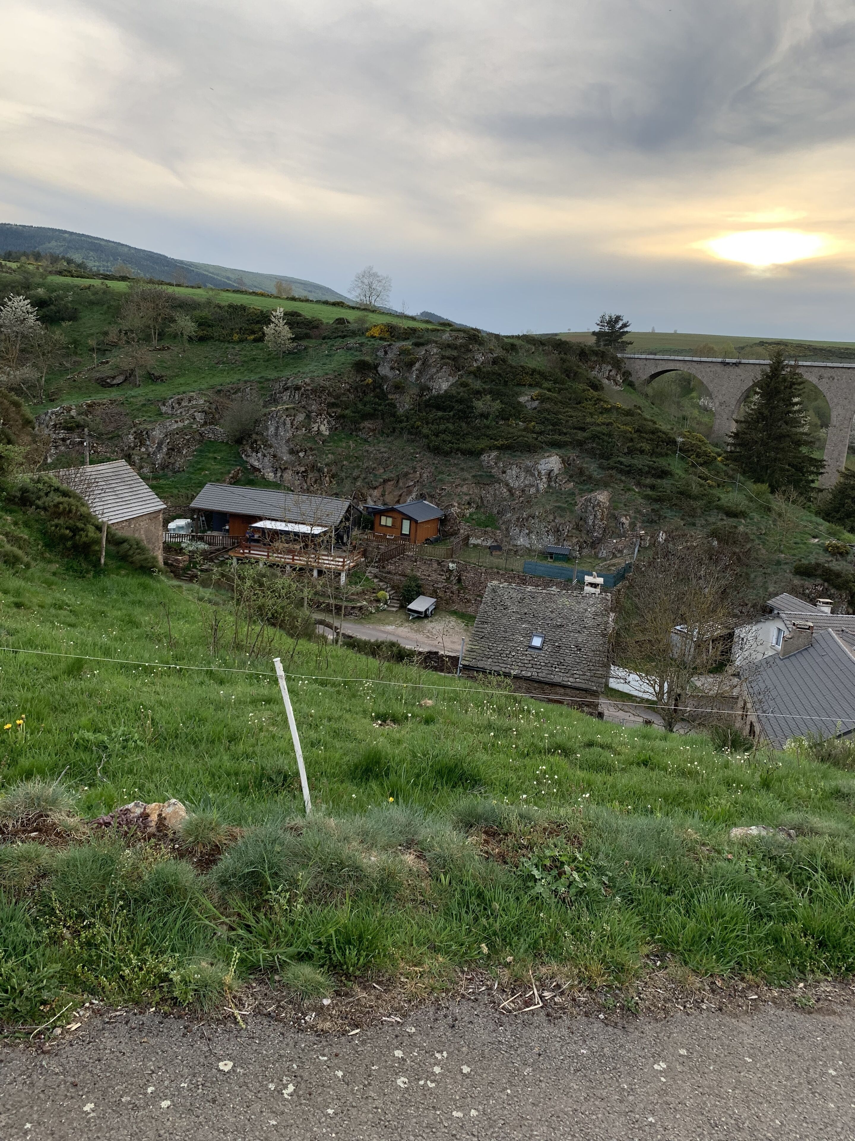 A rural landscape with a stone bridge, houses, and a grassy field.
