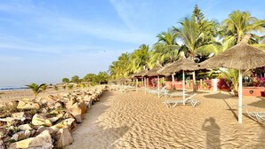 A beach with thatched umbrellas, lounge chairs, and palm trees. - Bookwithclass-luxury Stay Pool Villa am Meer (Saly Portudal)