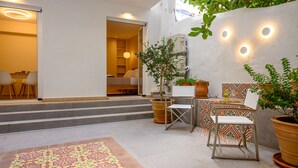 Un espace patio agrémenté d’un tapis à motifs, de meubles d’extérieur, de plantes en pot et d’un mur orné d’appliques lumineuses de forme circulaire.