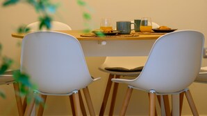 Un coin repas avec une table en bois, des chaises blanches et une plante en arrière-plan.