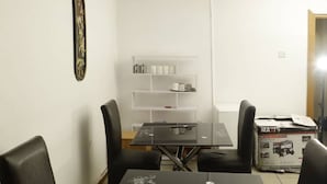 A dining area with a black table and four chairs, a white shelf with items, and a framed picture on the wall. - Calbert lodge Abuja (Abuja)
