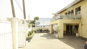 A courtyard with a covered seating area, a white fence, and a building with a balcony. - Calbert lodge Abuja (Abuja)