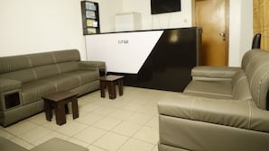 A living room with a sofa, a coffee table, and a recliner. There is a TV mounted on the wall and a door in the background. - Calbert lodge Abuja (Abuja)