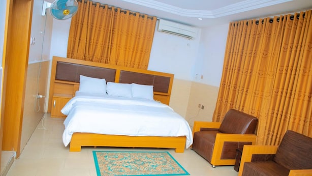 A hotel room with a bed, a chair, a fan, and curtains. - Calbert lodge Abuja (Abuja)