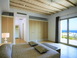 A bedroom with a bed, a walk-in closet, and a large window with a view of the ocean.